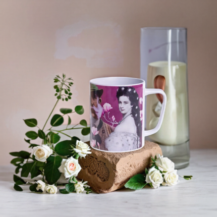 Weißer Keramikbecher mit kunstvollem Pop-Art-Druck einer historischen Dame, umgeben von weißen Rosen und Deko – inspirierendes Beispiel für einen Kaffeebecher mit Logodruck